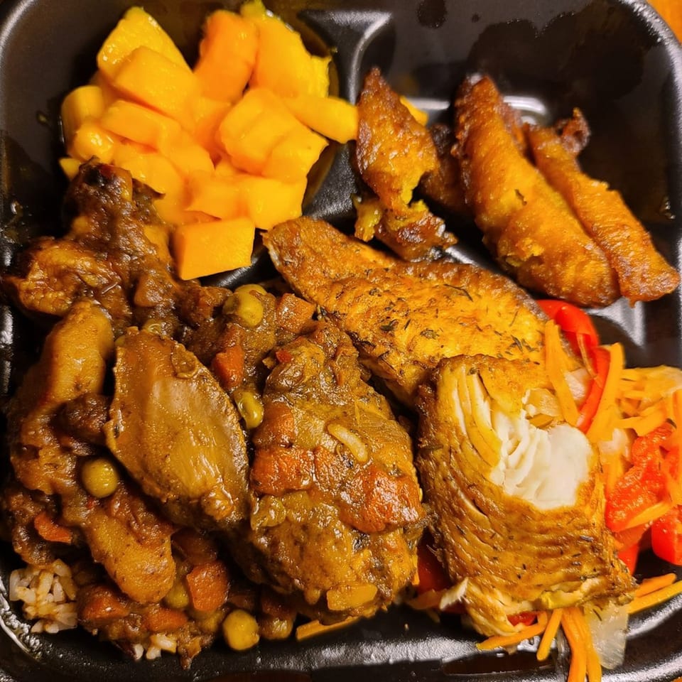 A Jamaican meal with curry chicken, fried fish, plantains, mango, and pickled vegetables.