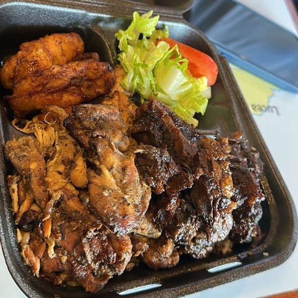A takeout container filled with Jamaican jerk chicken, brown stew chicken, plantains, and a side salad.